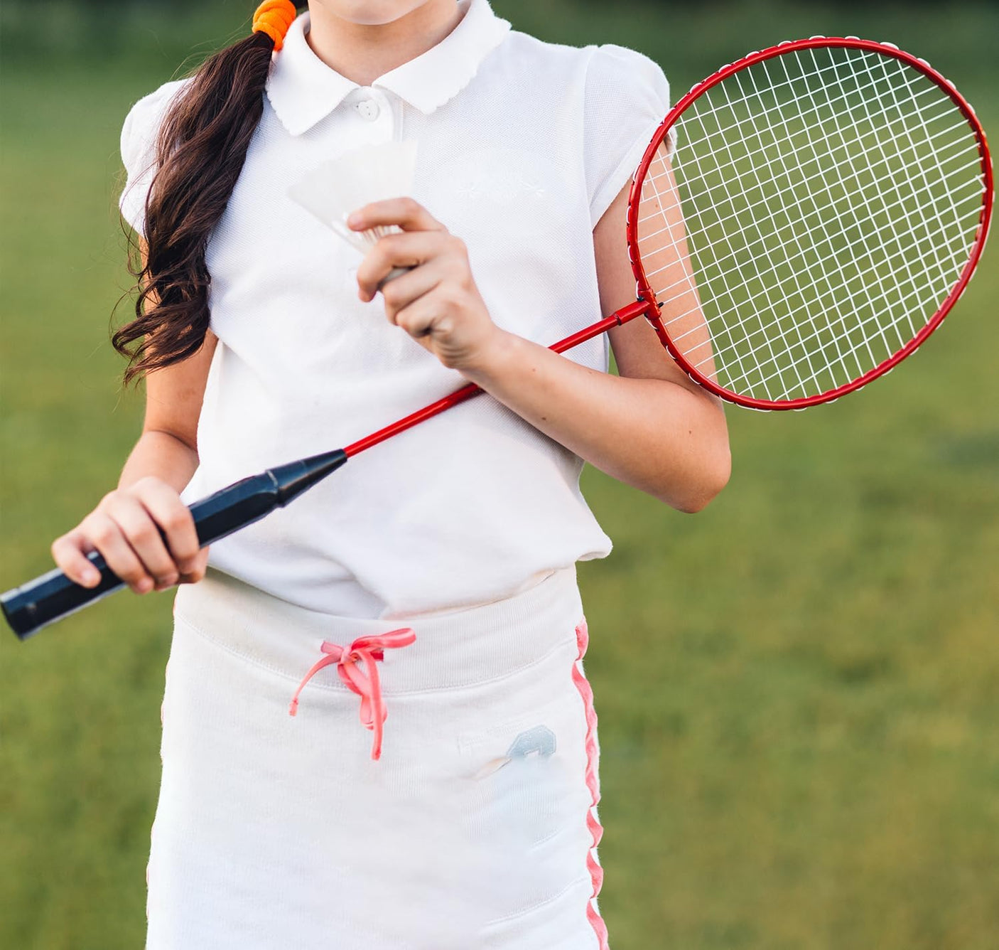 Person holding a red badminton racket on a grassy background