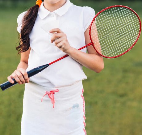Person holding a red badminton racket on a grassy background